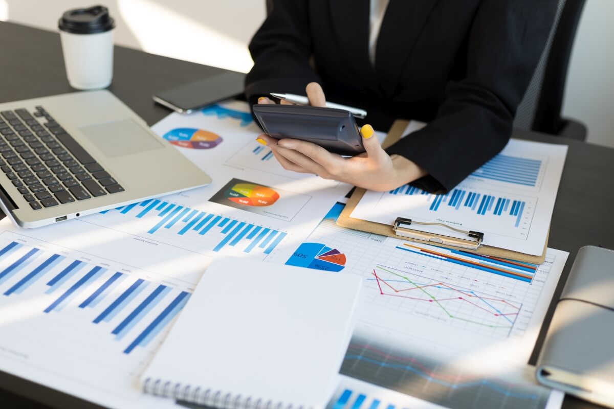 Osoba przy biurku przegląda raporty finansowe z kalkulatorem, świadcząc usługi księgowe.