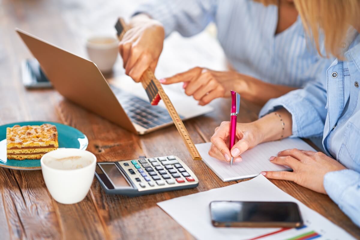 Dwie osoby pracują przy biurku z laptopem i kalkulatorem, oferując usługi rachunkowe.